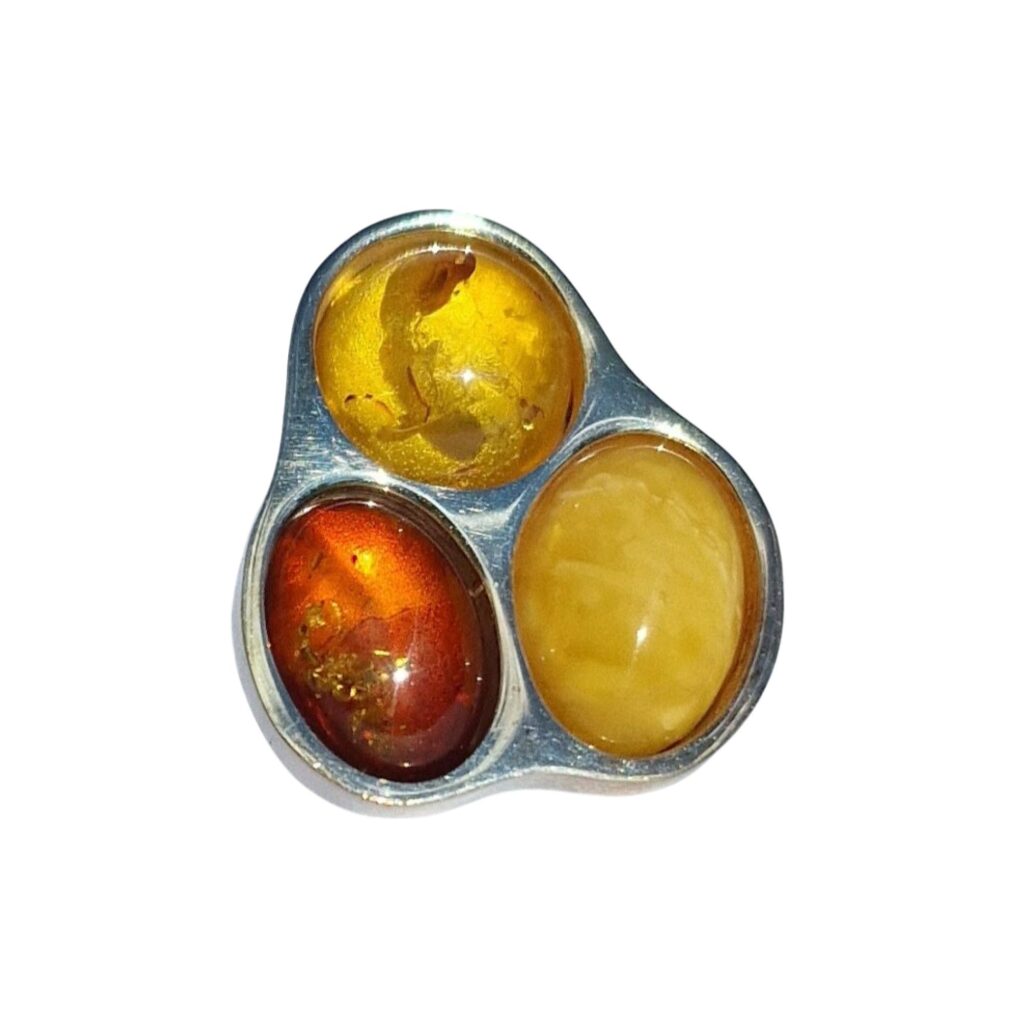 A BOLD TRILOGY OF AMBER BEAUTY, this piece features honey-colored, cognac, and milky amber stones in a shimmering silver setting, elegantly arranged in a triangular design to showcase their captivating allure.