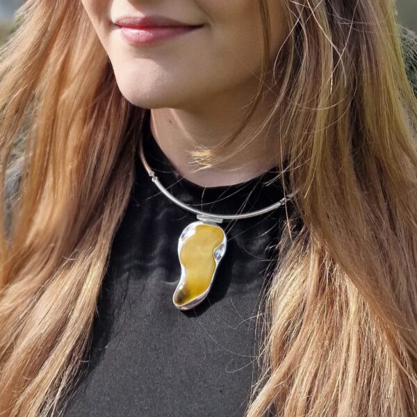 A person wearing a black top and the Butterscotch Amber Choker Necklace with a large, irregularly shaped amber pendant.