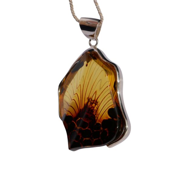 The CARVED AMBER ART PENDANT elegantly features an amber-like stone with a captivating insect inclusion, beautifully framed in silver and hung on a chain.