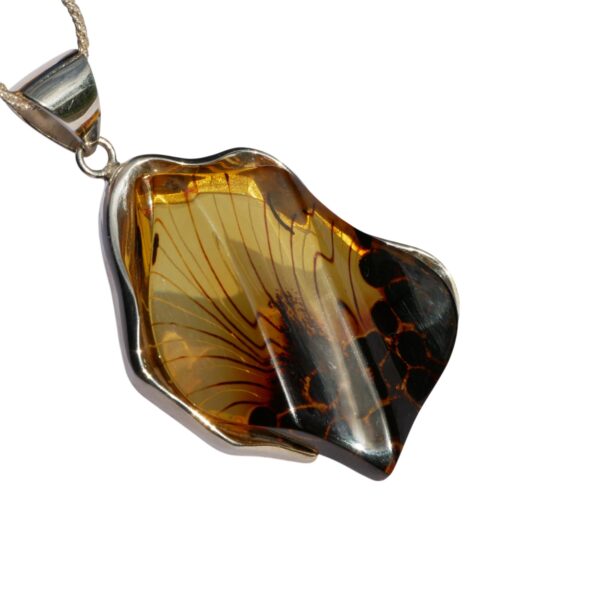 The CARVED AMBER ART PENDANT features an abstract amber-colored gemstone with dark marbled patterns, set in a sleek silver frame and hanging elegantly on a chain.