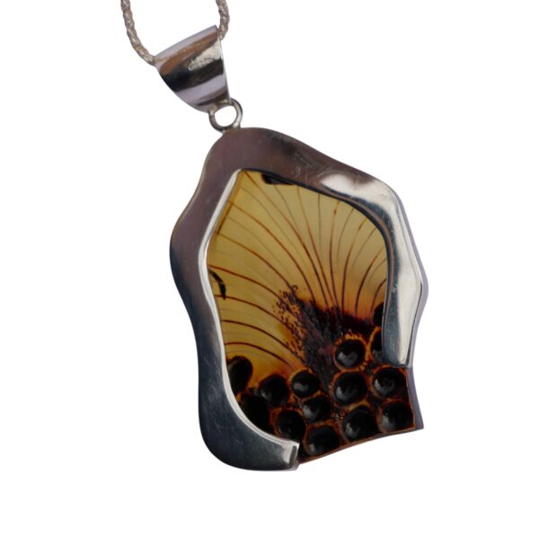 The CARVED AMBER ART PENDANT elegantly displays a floral design amber centerpiece, gracefully hanging from a chain.