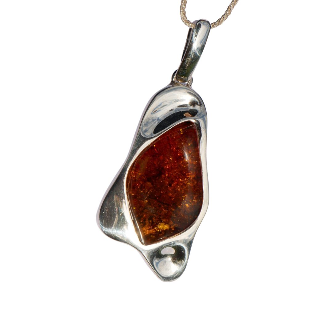 The CHUNKY COGNAC AMBER PENDANT IN SOLID SILVER features an abstract design with a radiant amber stone in the center, hanging from a thin chain.