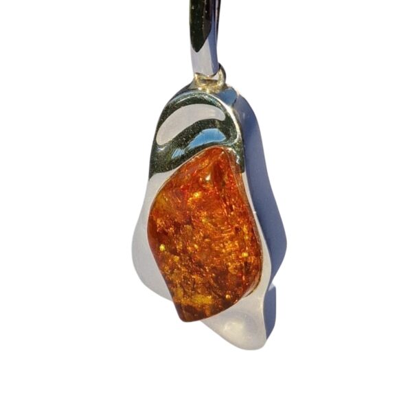 The CHUNKY COGNAC AMBER PENDANT IN SOLID SILVER captures attention with its irregular amber stone, shimmering with golden flecks.