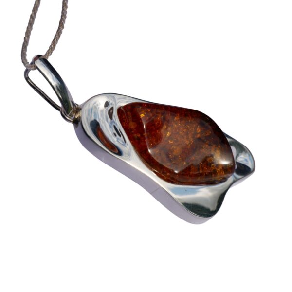 The CHUNKY COGNAC AMBER PENDANT IN SOLID SILVER beautifully showcases a rich amber stone that glows warmly against a white background.