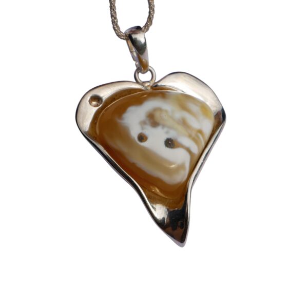 The ETERNAL HEART pendant showcases a heart shape with a brown and white swirl pattern resembling rare Baltic amber, two small black dots, and is elegantly set in silver, suspended from a chain.