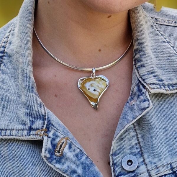 A person wearing a denim jacket and the ETERNAL HEART: RARE BALTIC AMBER & SILVER PENDANT, featuring a heart-shaped amber.