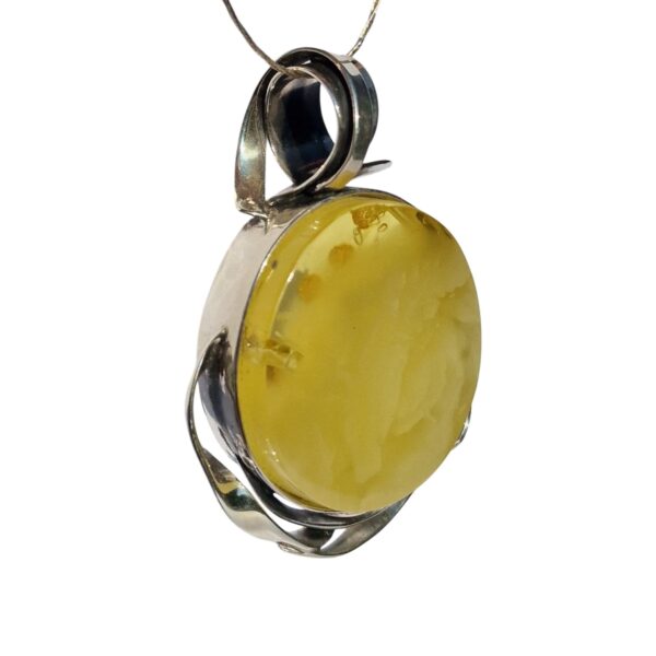 The HANDCRAFTED CHUNKY SILVER & YELLOW AMBER PENDANT features a beautifully set round amber stone in a silver swirl design, elegantly hanging from a thin wire.