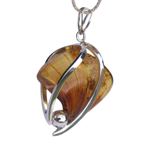 The NATURE'S SCULPTED AMBER pendant features a polished amber stone in a silver setting, adorned with abstract metal curves and a small silver sphere, capturing nature's warmth and artistry.